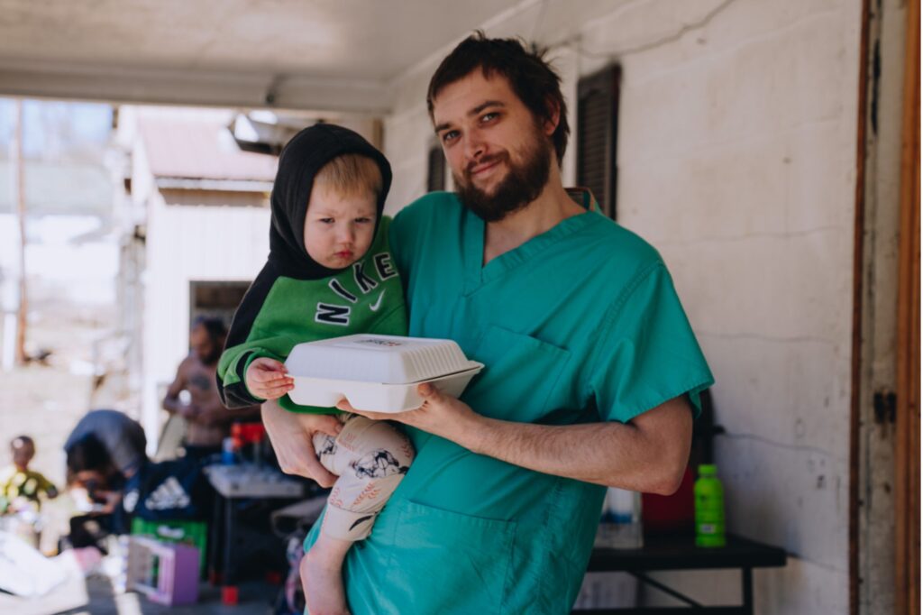 A father receiving a Mercy Chefs meal while holding his son in the aftermath of the Kentucky floods.