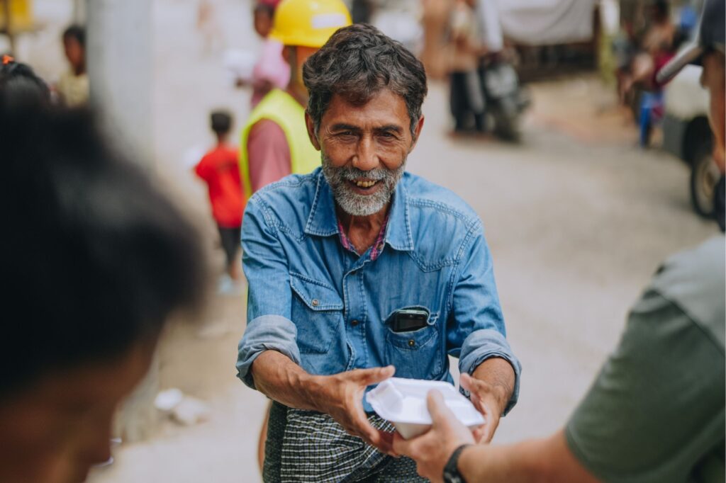 A man receiving a hot meal with joy in the aftermath of the 7.7. earthquakes in Myanmar.