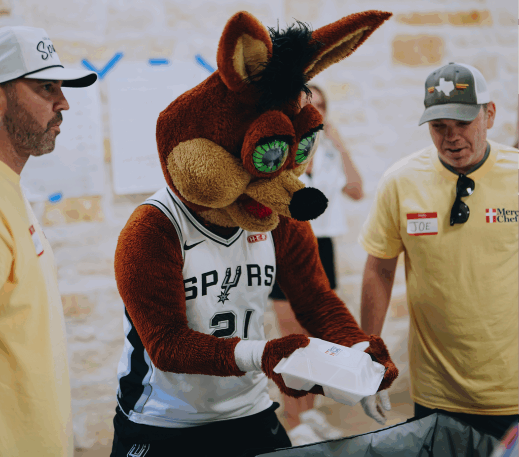 The Spurs Coyote mascot placing meals into Sterno bags for distribution