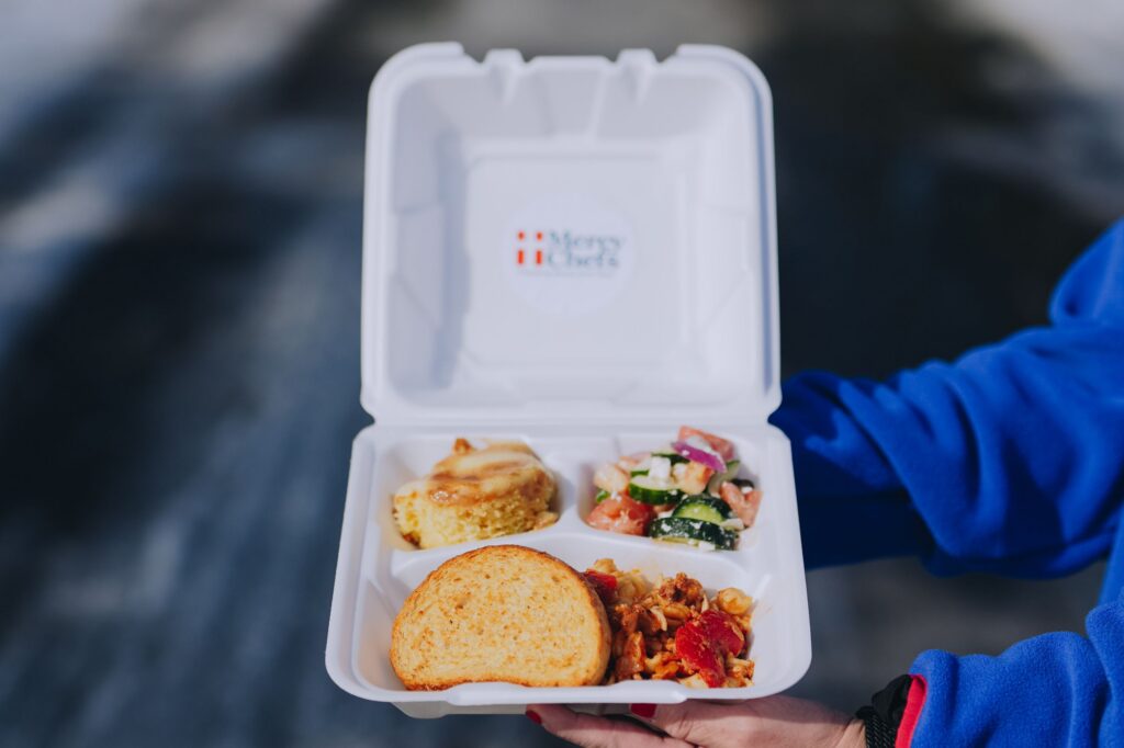 A hot plate of Italian chicken pasta with fresh salad and garlic bread, prepared by Mercy Chefs